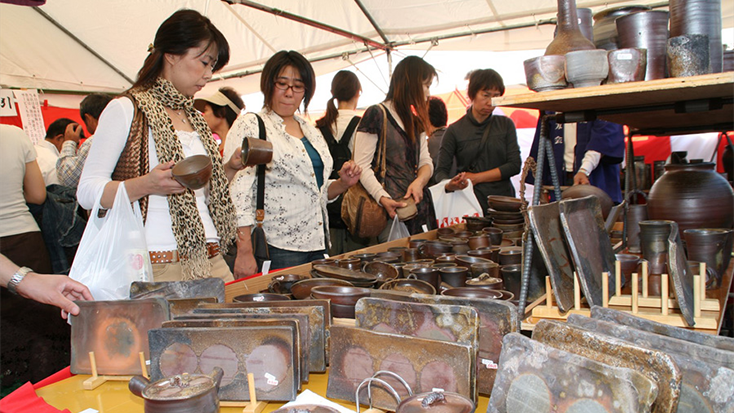 A group of people standing under a Bizen Pottery Festival tent shopping for bizenyaki