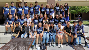 Group of students in matching blue "asb" shirts posing together on outdoor school benches, sunny day.