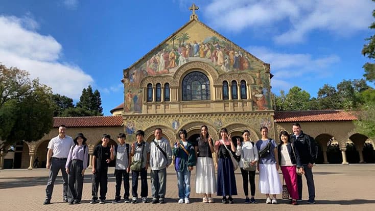 A group of people stand in a line posing for a photo in front of a large, ornate church with a colorful mural on its facade.